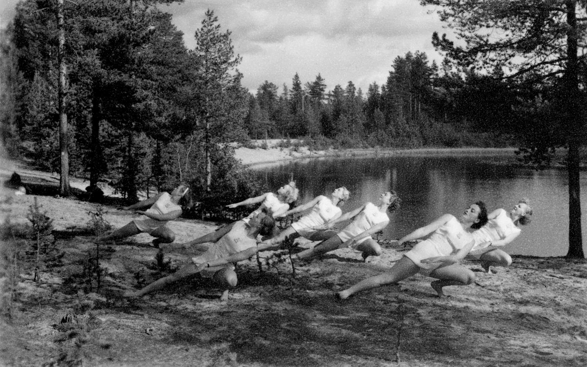 Kvinnliga gymnaster i vackra poser vid en skogstjärn.