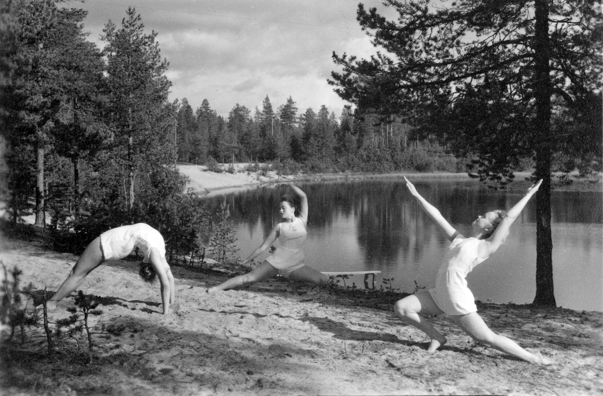 Kvinnliga gymnaster i vackra poser vid en skogstjärn.