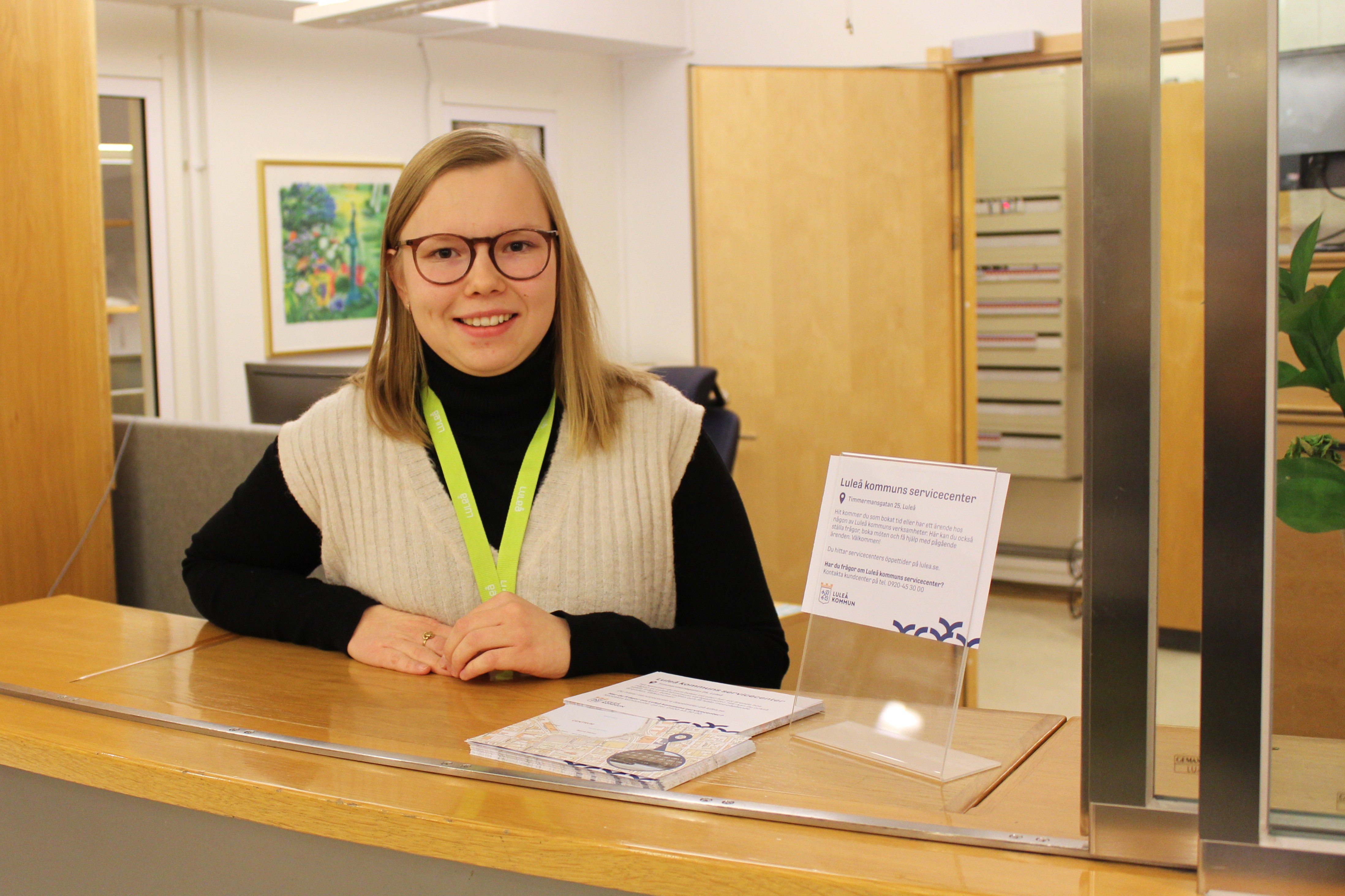 Ellen står bakom informationsluckan i en reception. Hon ler.