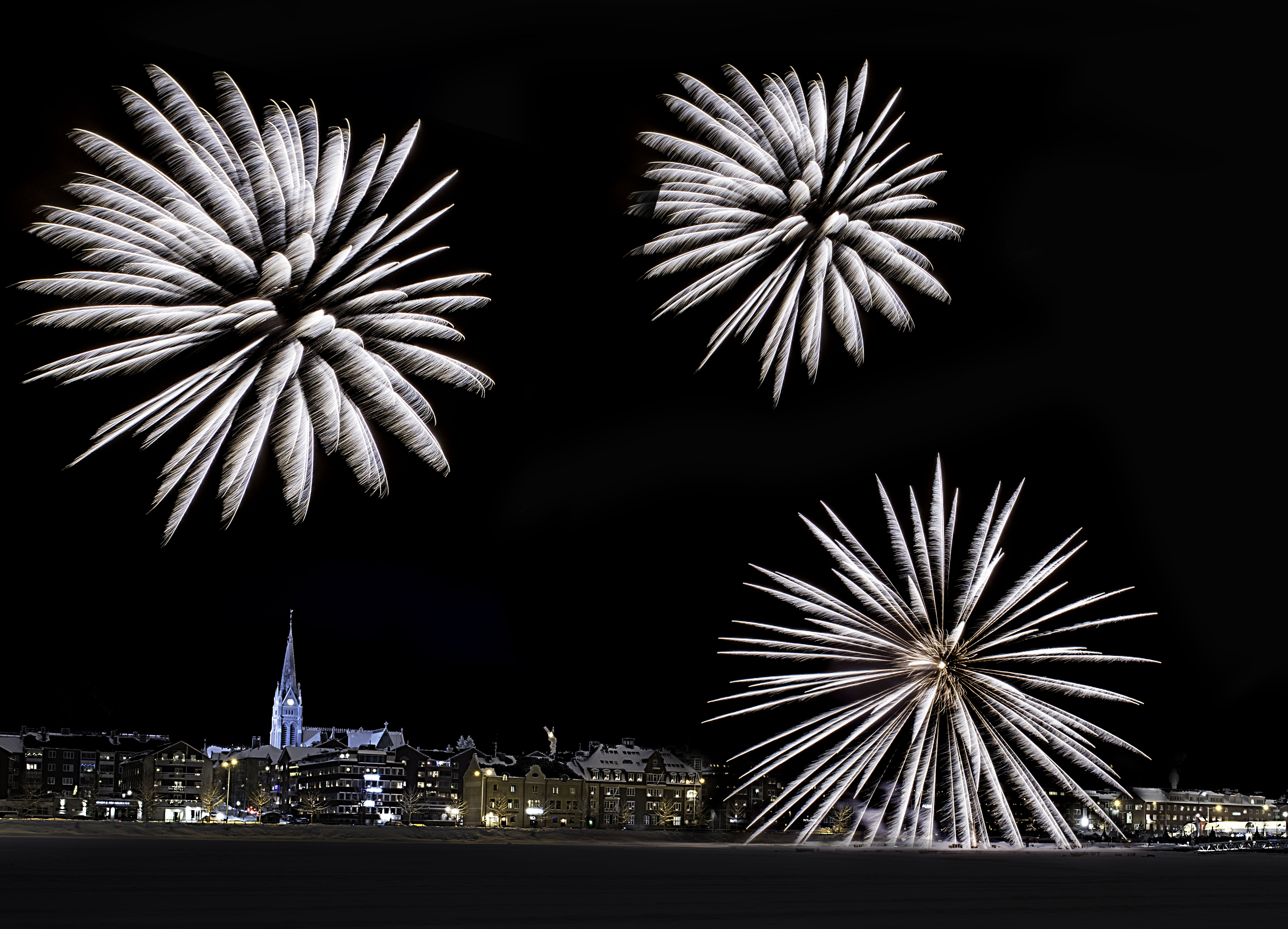 Fyrverkerier över Södra hamn 2017. En svart natthimmel med stora vita raketer som blommor.