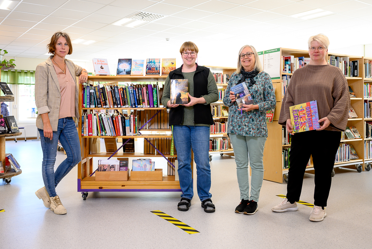 Personalen på Björkskatans bibliotek står framför en bokhylla och håller i böcker.