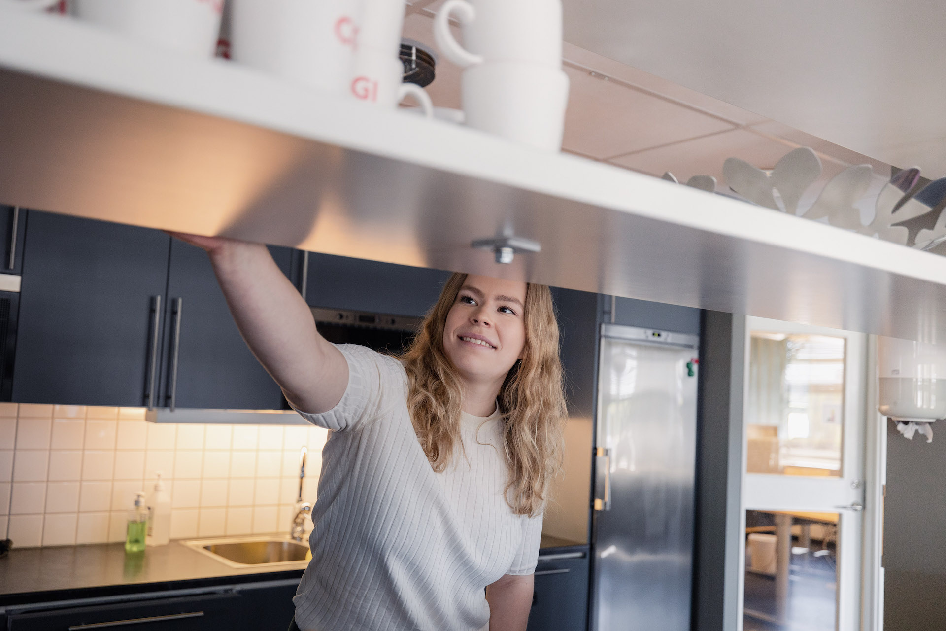 Julia Jones sträcker sig efter en kaffekopp i köket på kontoret