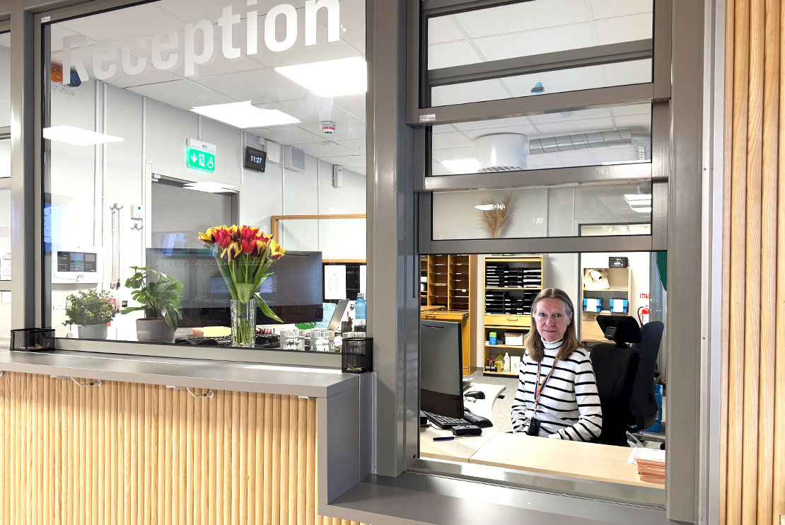 Carola Lundgren, administratör, sitter i en reception med träpanel och glas. Det är Servicecenters reception.