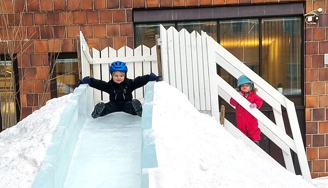 En liten kille vågar åka själv nedför isrutschkanan. Håller ut armar och ben för att det inte ska gå så fort.