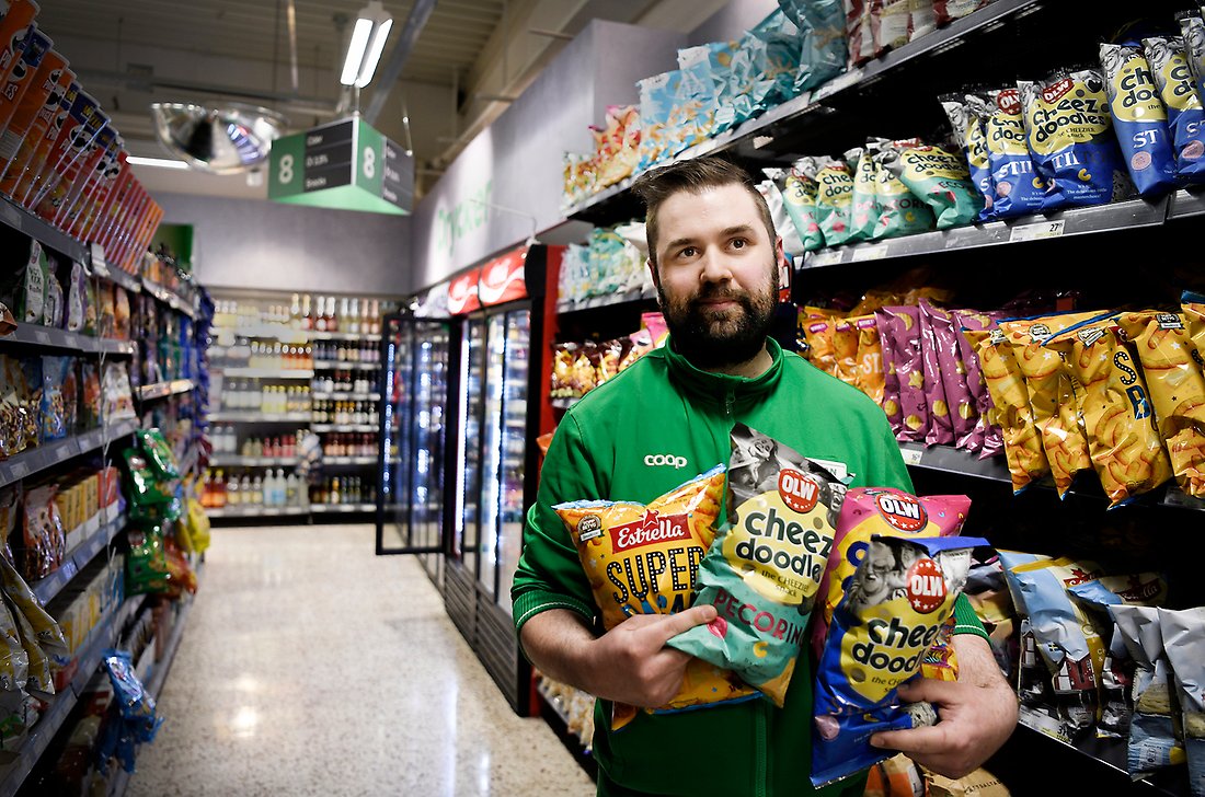 En kille i mörkt hår står framför en färgglad välsorterad chipshyllan