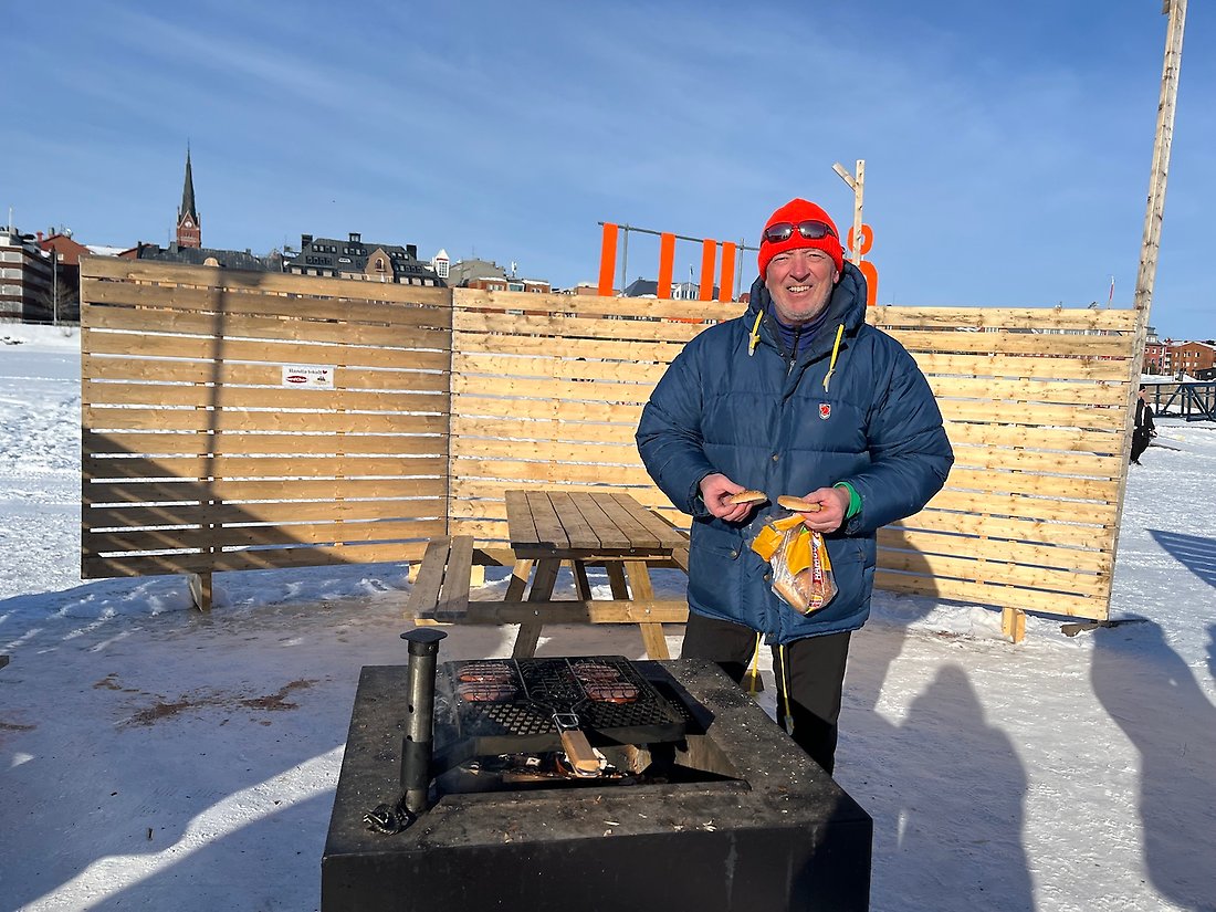 En man vid en grill i solen på isvägen. Han grillar parisare.