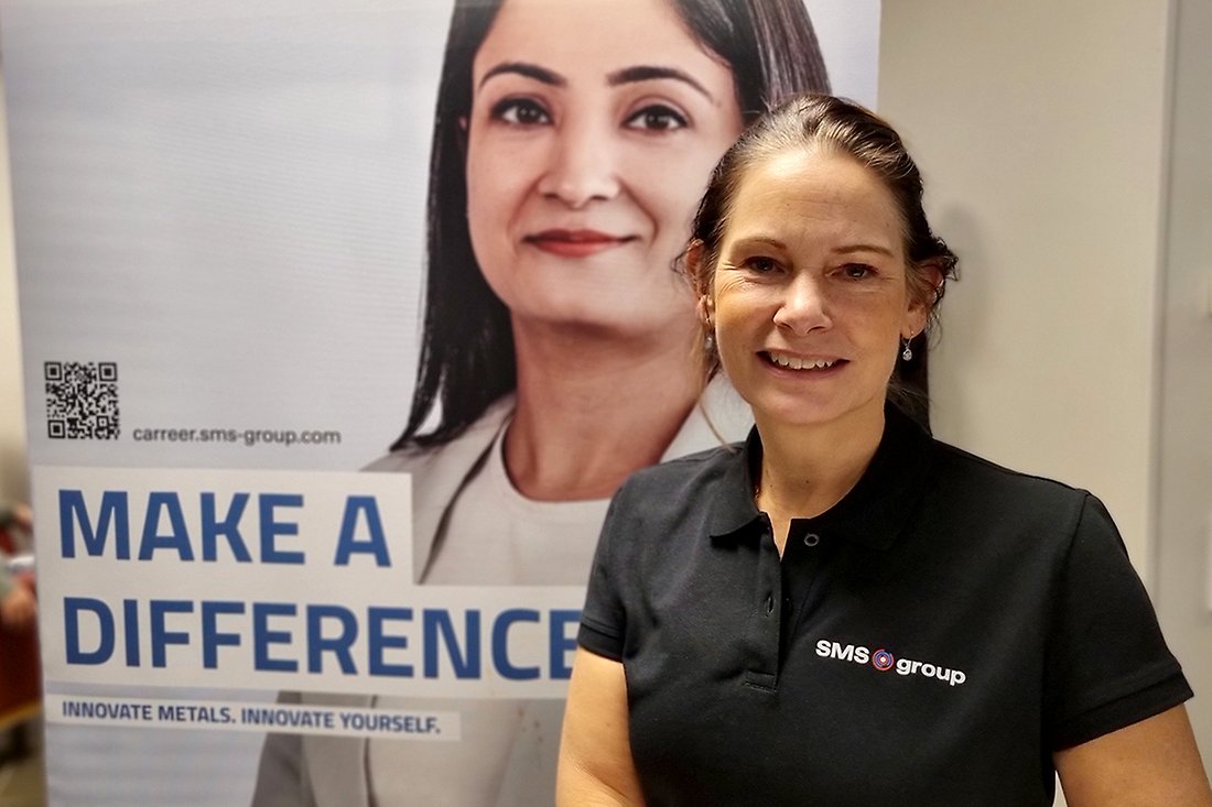 Leende kvinna med emblem på tröjan där det står SMS Group