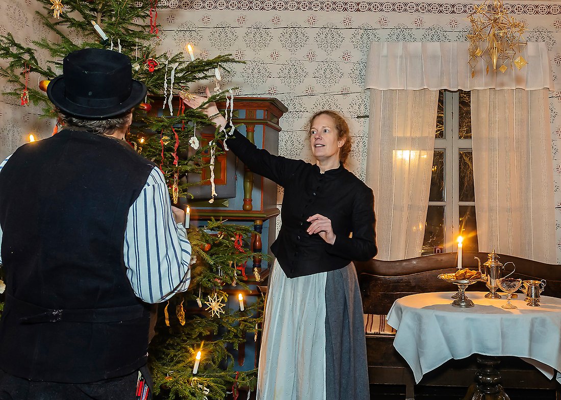 Erica Rönnbäck, museipedagog Hägnan, visar en julstjärna som hänger i en julgran för en man. Båda är klädda i gamla kläder. Han i väst och hon i långkjol.